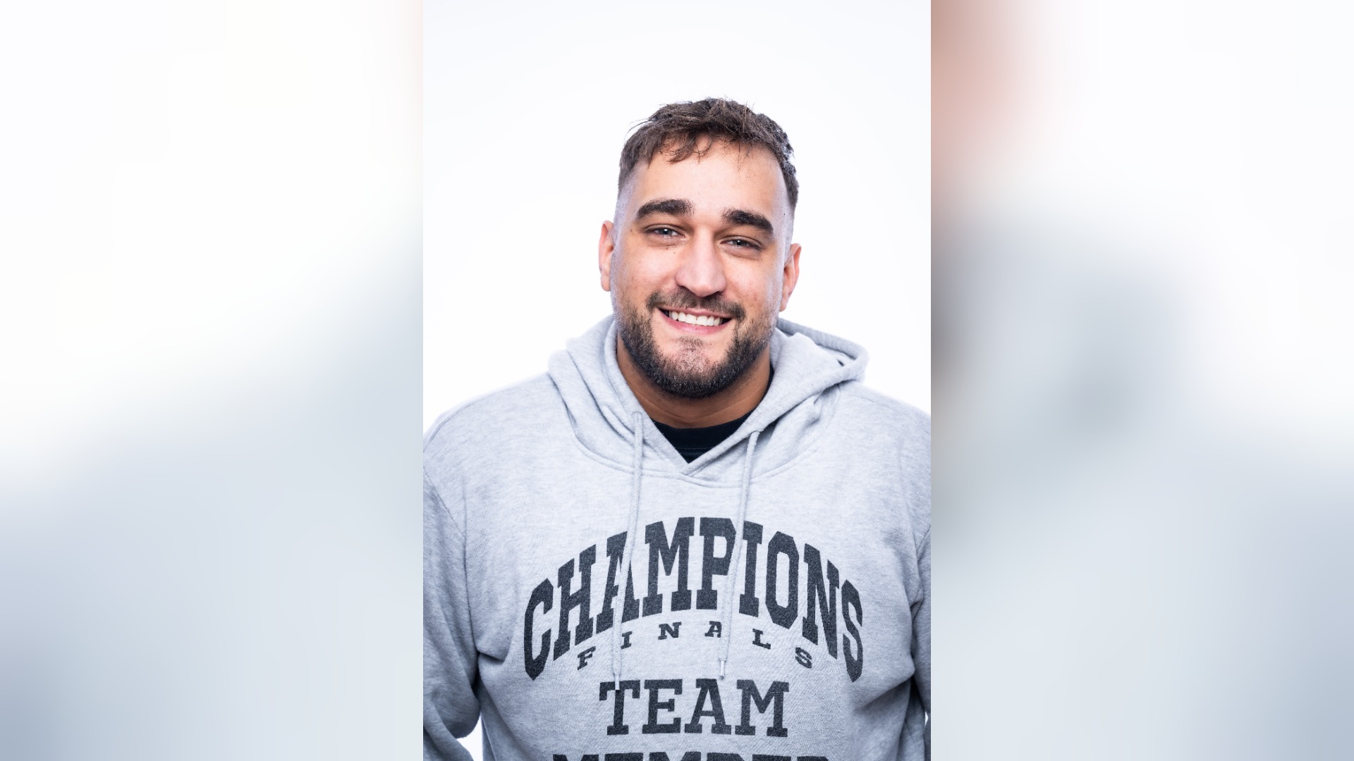 KARLITOZ lächelt in einem grauen Hoodie mit der Aufschrift "Champions Finals Team Member" direkt in die Kamera