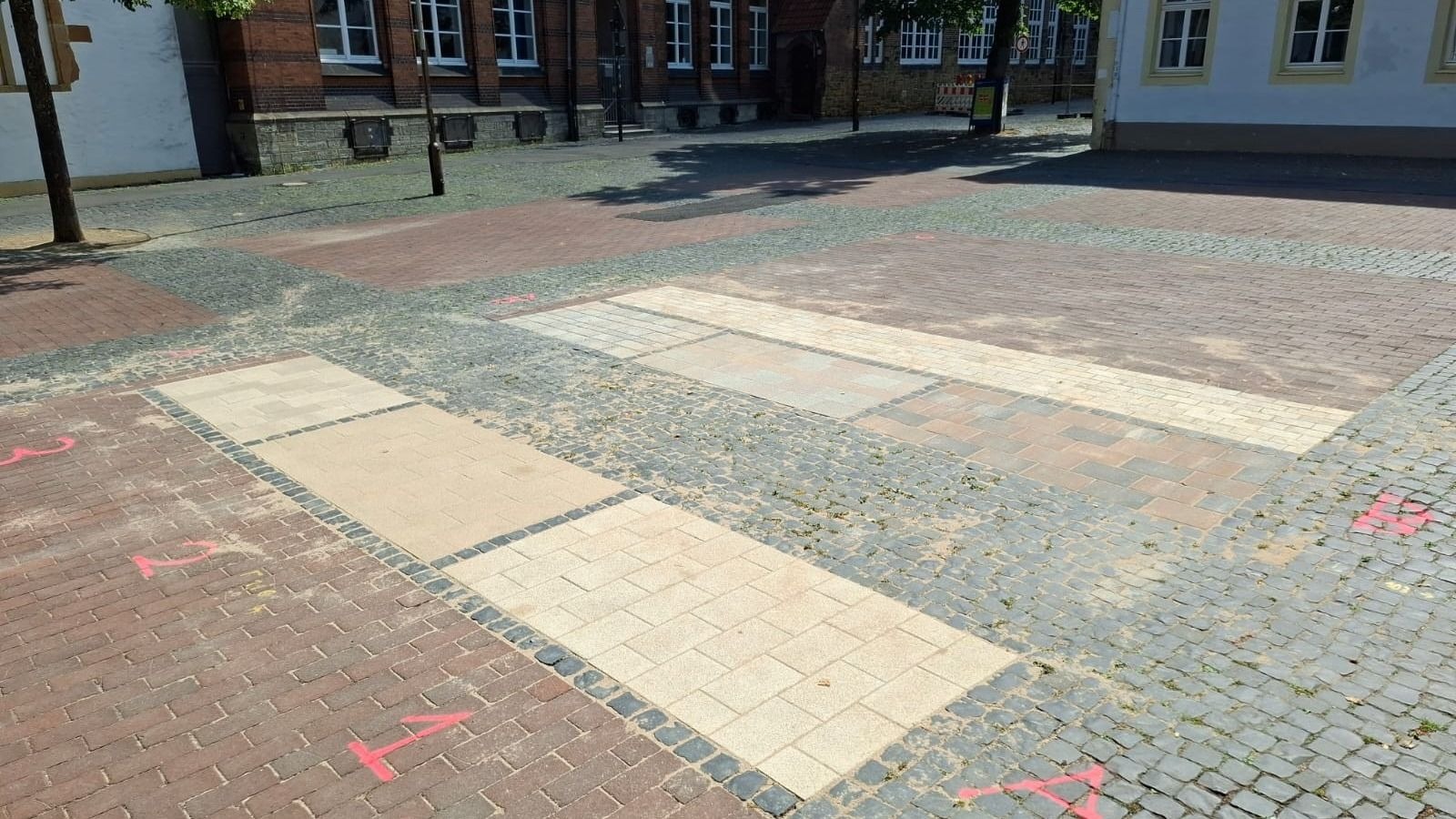 Mehrere Pflaster-Musterflächen aus verschiedenen Steinen auf dem Klosterplatz, mit roten Markierungen am Boden und