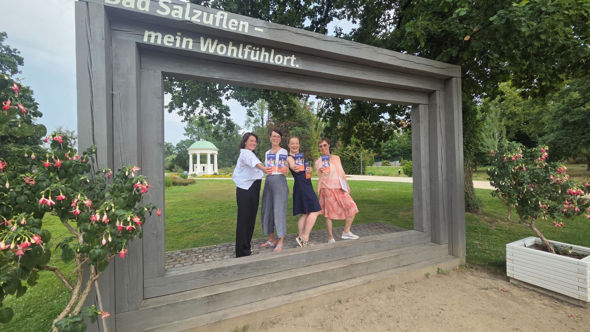 Vier lächelnde Frauen präsentieren Programmhefte in einem großen Holzrahmen mit der Aufschrift Bad Salzuflen in einem