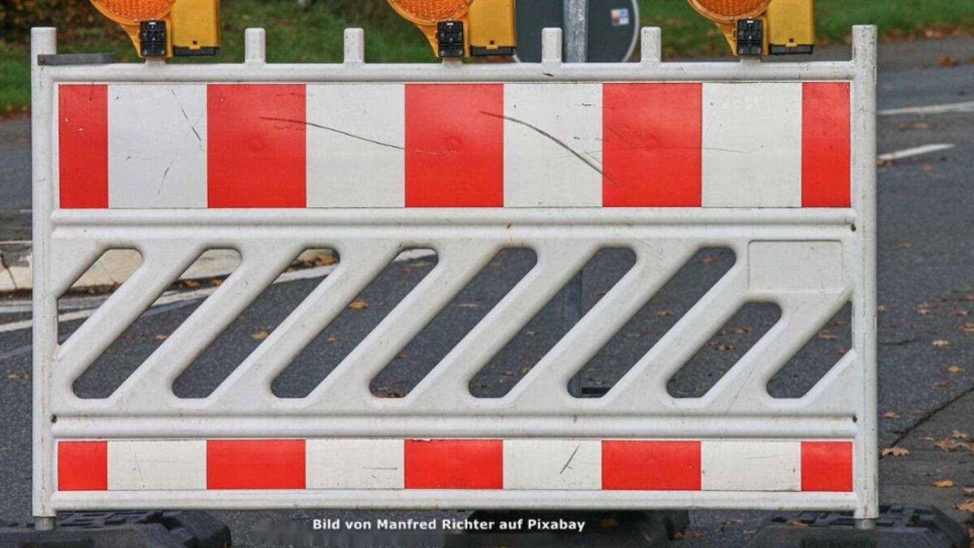 Rot-weiß gestreifte Baustellenabsperrung mit gelber Warnleuchte auf dunklem Asphalt