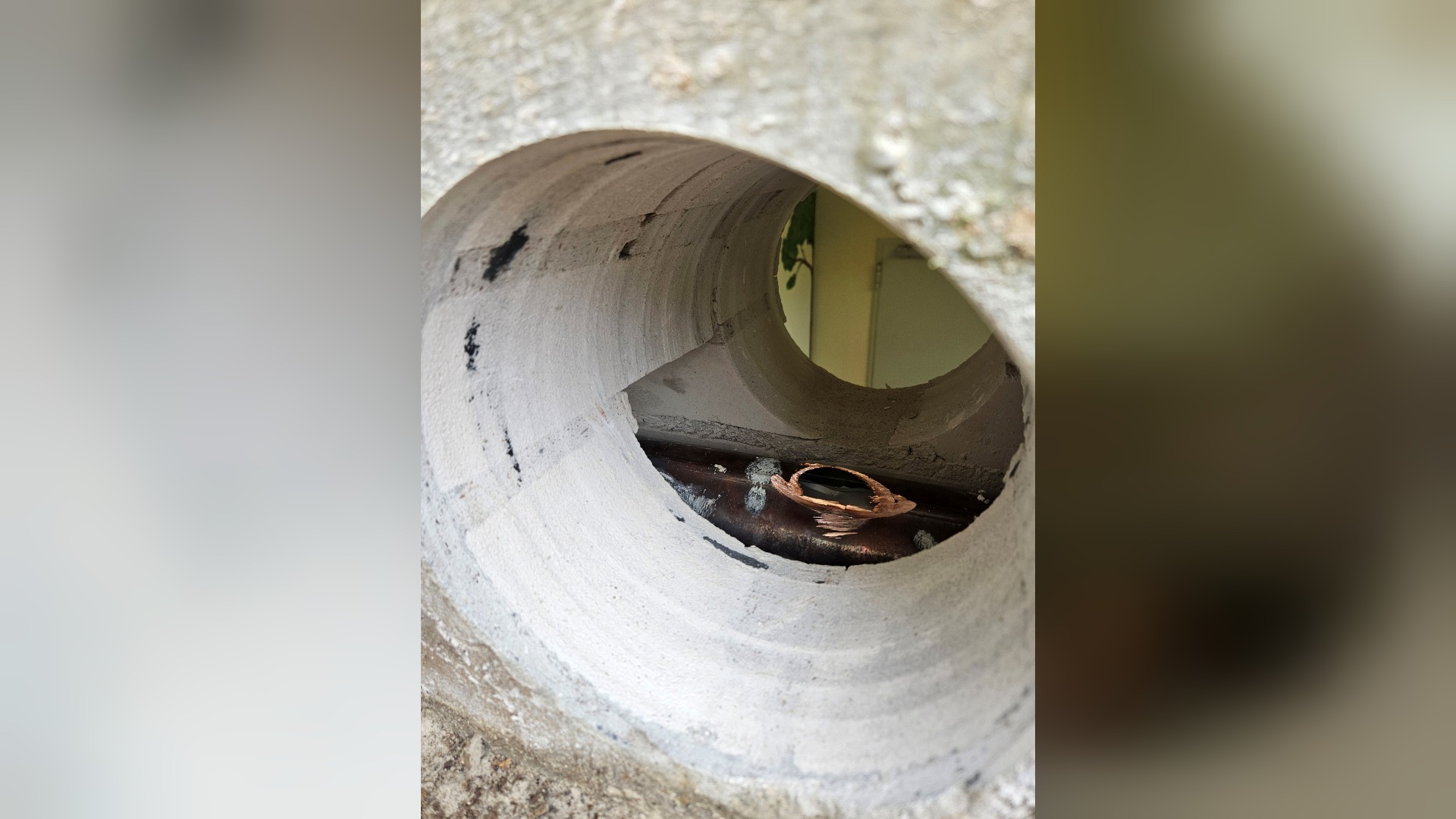 Blick in ein rundes Loch im Beton, in dem ein aufgeschnittenes dunkles Metallrohr liegt