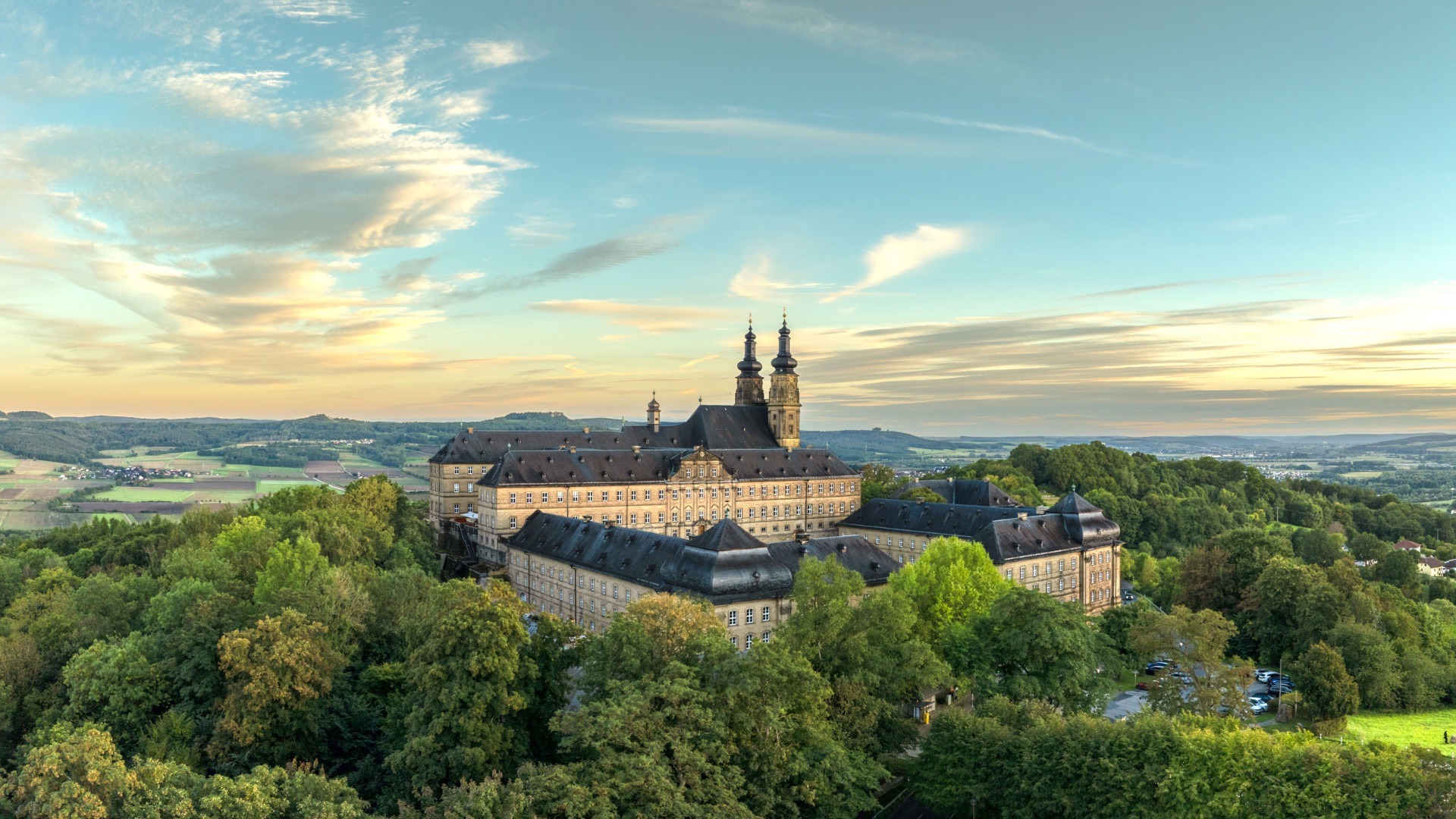 Kloster Banz mit seinen zwei Türmen, umgeben von Wäldern und einer weiten Landschaft unter einem teilweise bewölkten