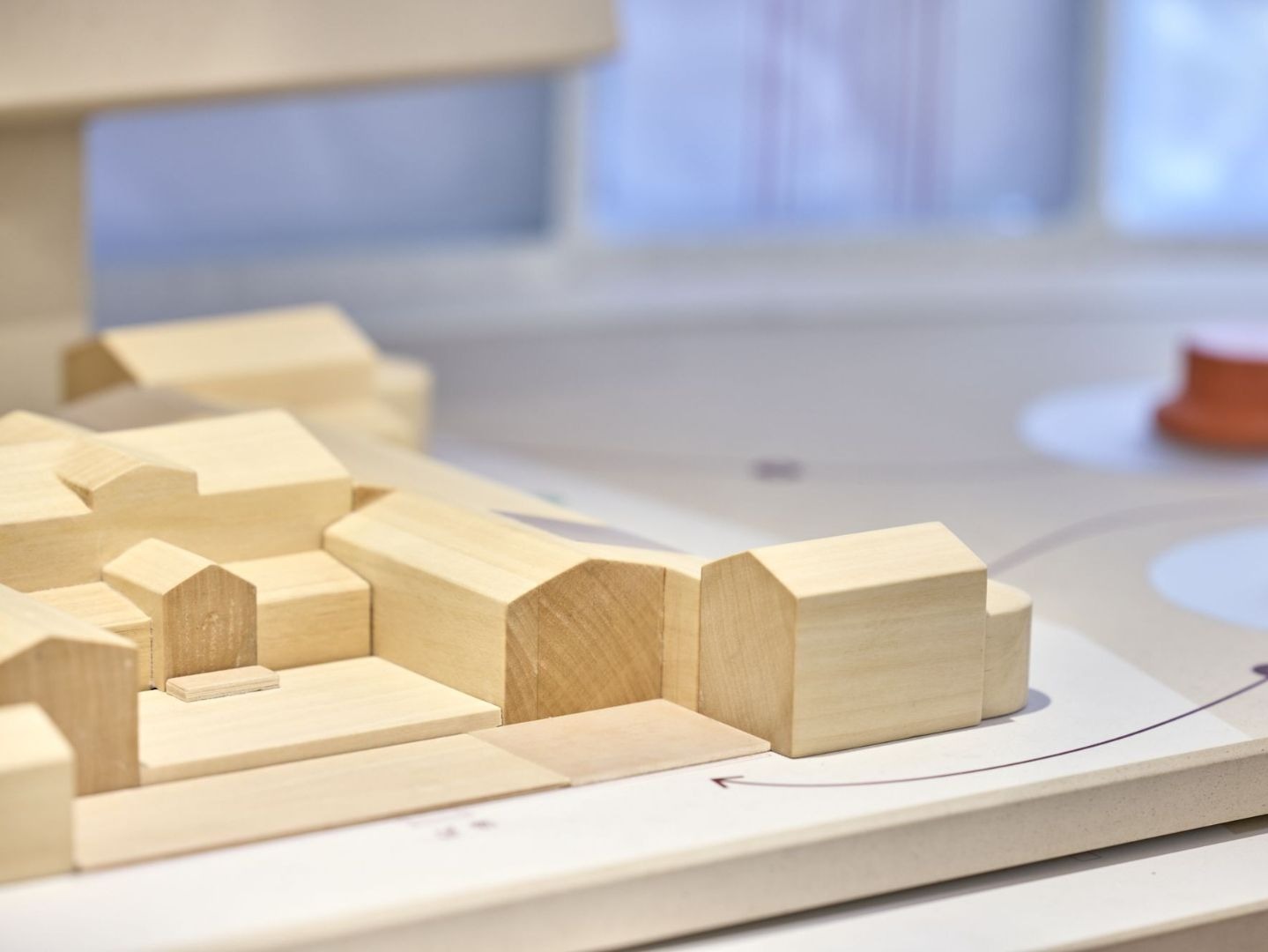 Holzmodell mit mehreren kleinen Gebäuden und Wegen auf einer hellgrauen Platte mit runden orangefarbenen Objekten