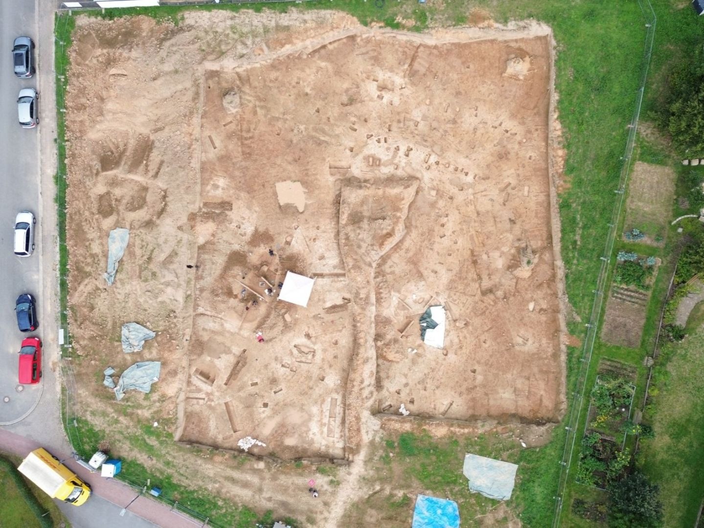 Große archäologische Ausgrabungsstätte mit freigelegten Fundamenten eines Hofes, Arbeitern, umgeben von Straße und