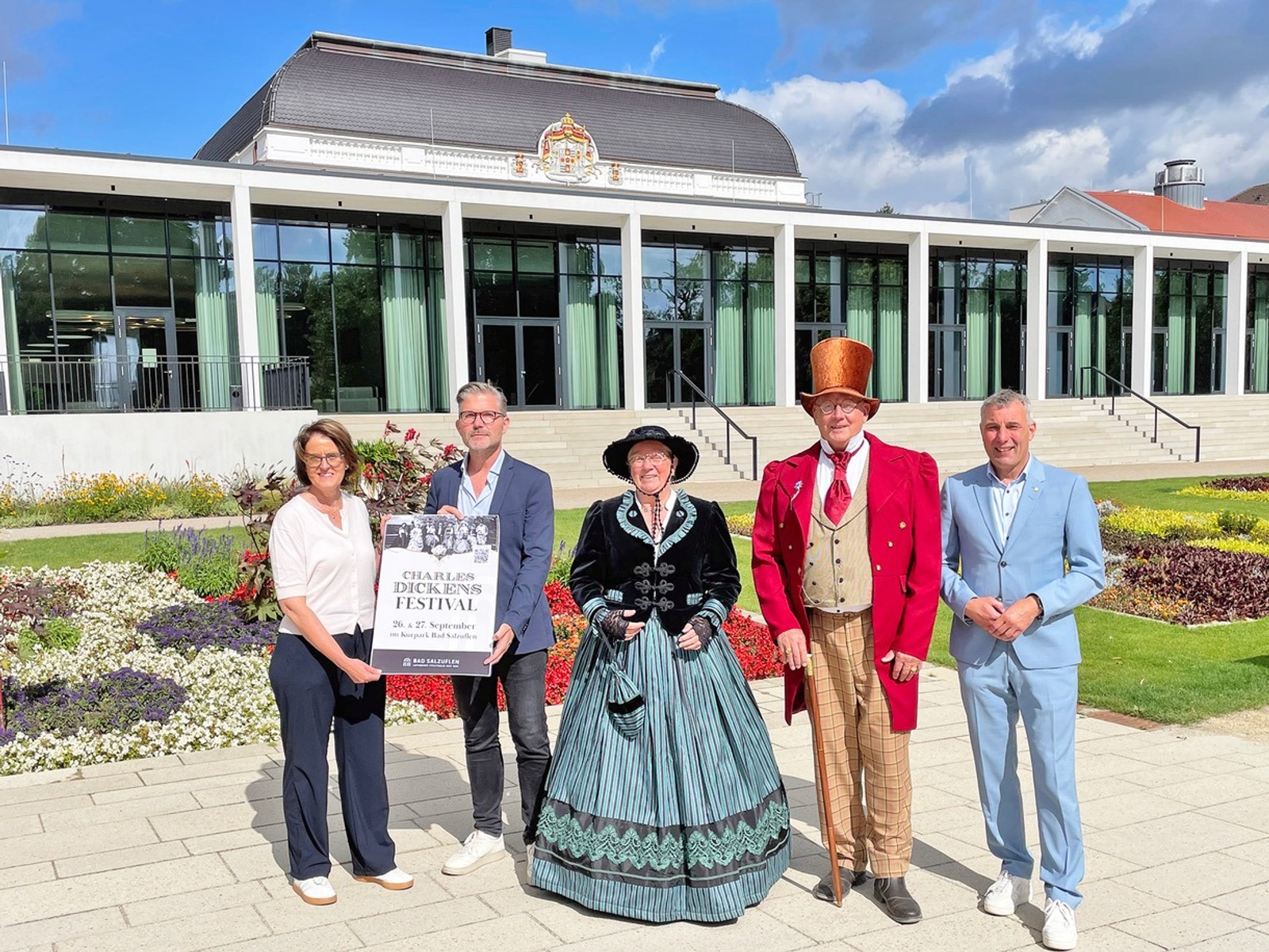 Fünf Personen, zwei davon in historischen Kostümen, stehen im Kurpark Bad Salzuflen vor einem Gebäude und halten ein