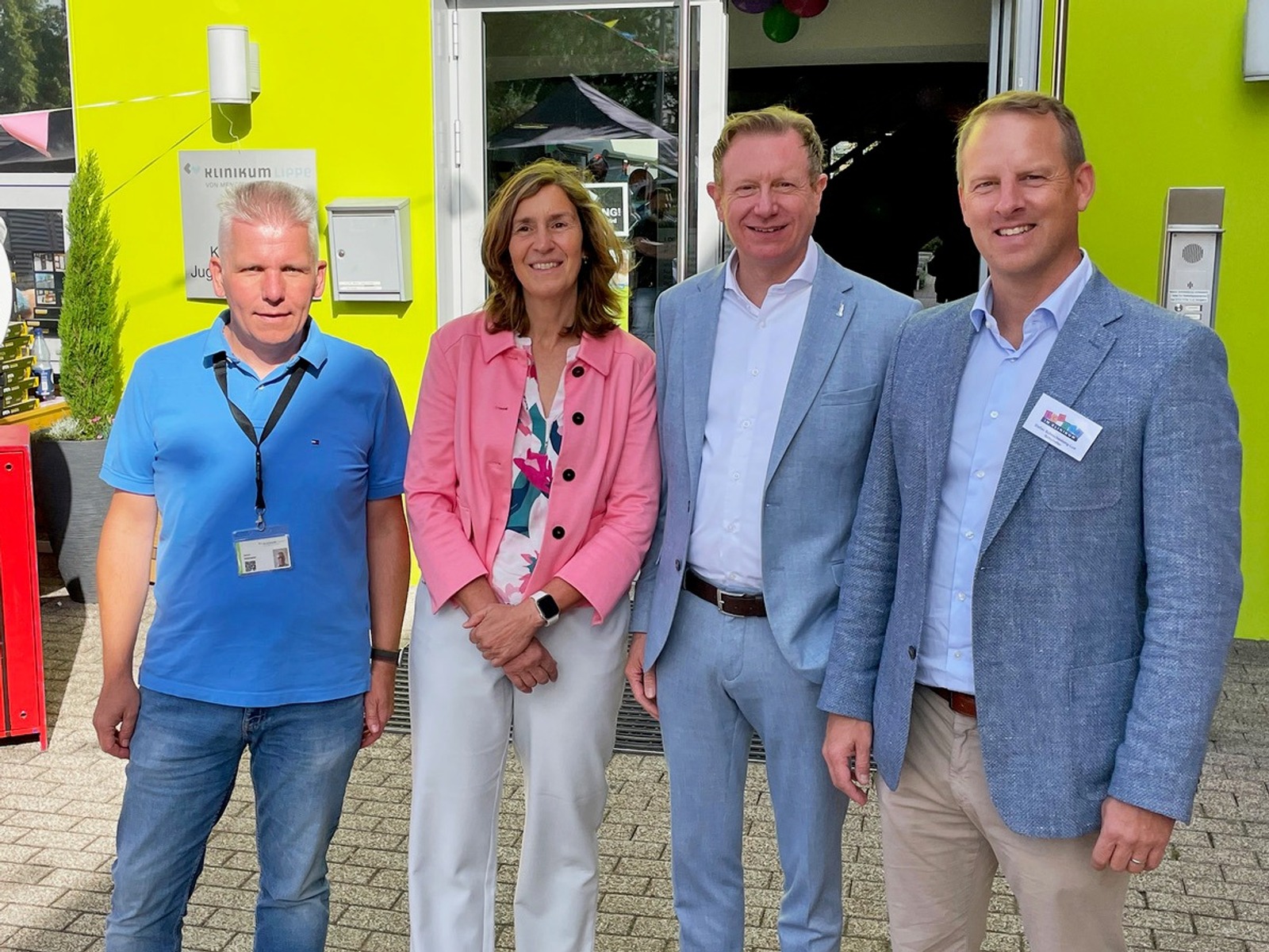 Vier Personen, drei Männer und eine Frau, lächeln vor dem Eingang der Kinderpsychiatrie Salzuflen