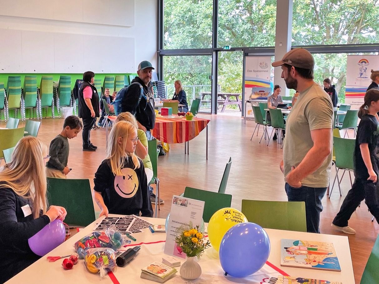 Aktionstag für Familien in einem großen Raum mit Kindern, Erwachsenen, Tischen, Luftballons und Bastelzeug