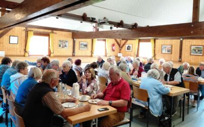 Zahlreiche Senioren sitzen in einem holzgetäfelten Raum an Tischen, trinken Kaffee und unterhalten sich lebhaft