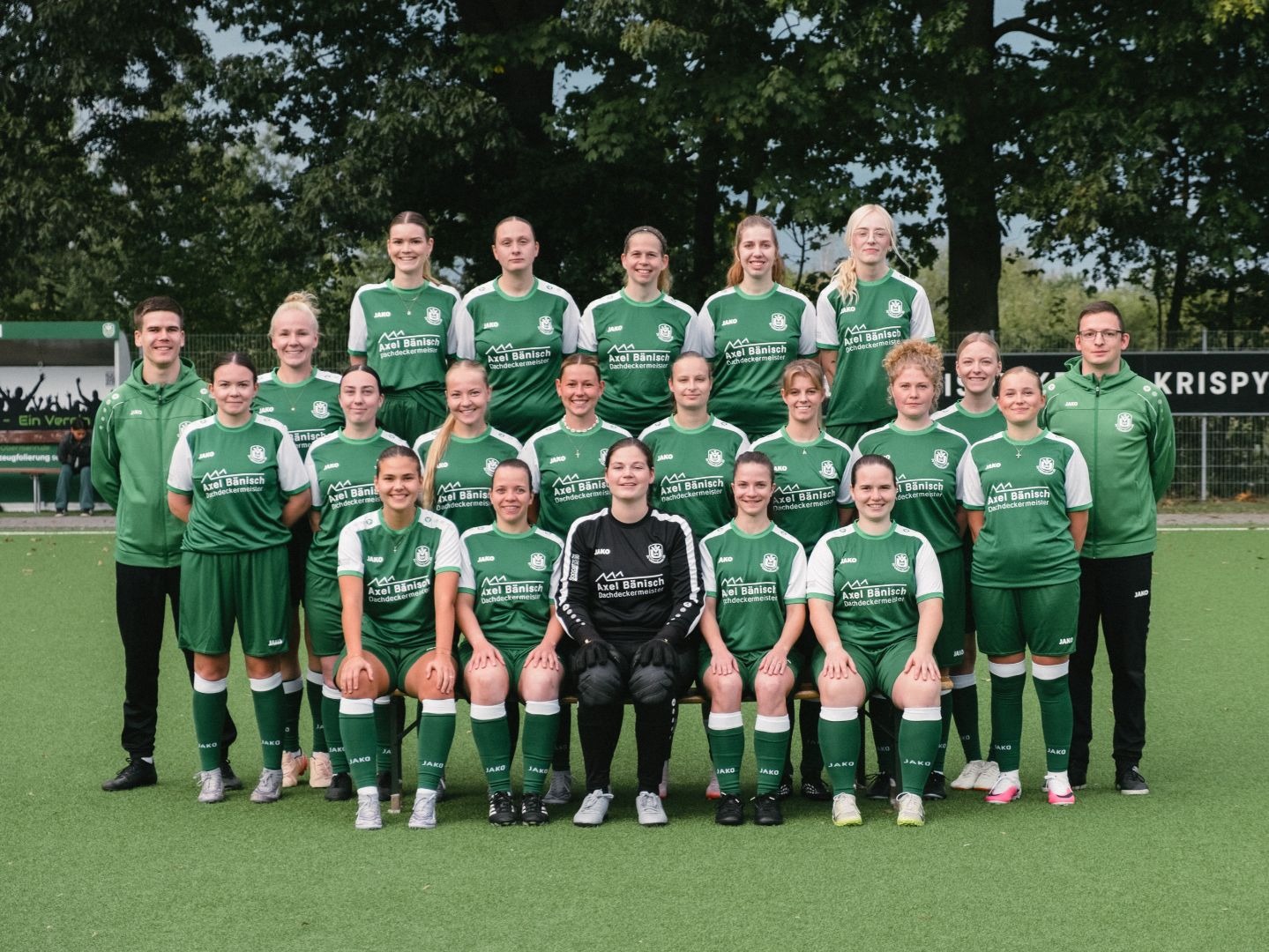 Die Ubbser Damenmannschaft in grünen Trikots mit zwei Trainern steht auf einem Fußballplatz