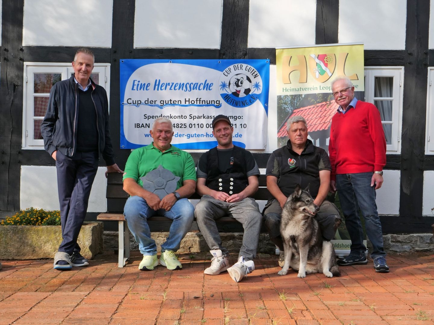 Fünf Männer und ein Hund vor einem Fachwerkhaus, mit Banners zum „Cup der guten Hoffnung“ und „Heimatverein