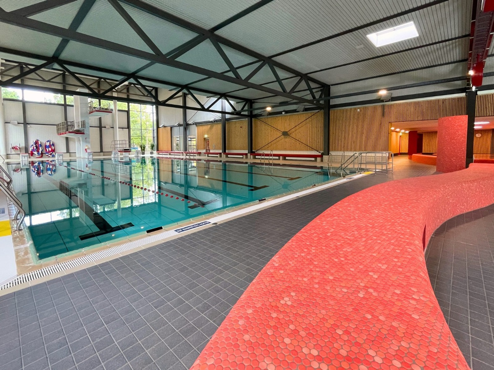Leeres Schwimmbecken im Lohfeld Bad mit Sprungturm, Startblöcken und einer geschwungenen roten Wand
