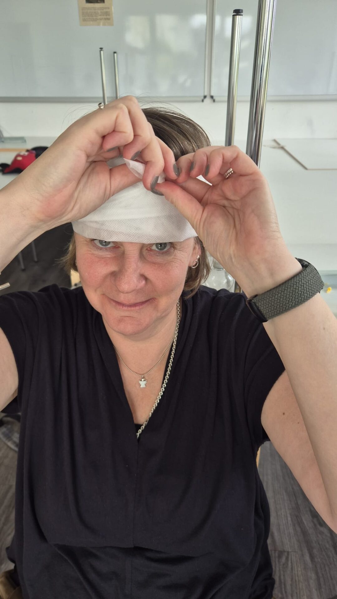 Frau legt bei einem Erste-Hilfe-Kurs einen weißen Verband an ihre Stirn an und blickt lächelnd in die Kamera