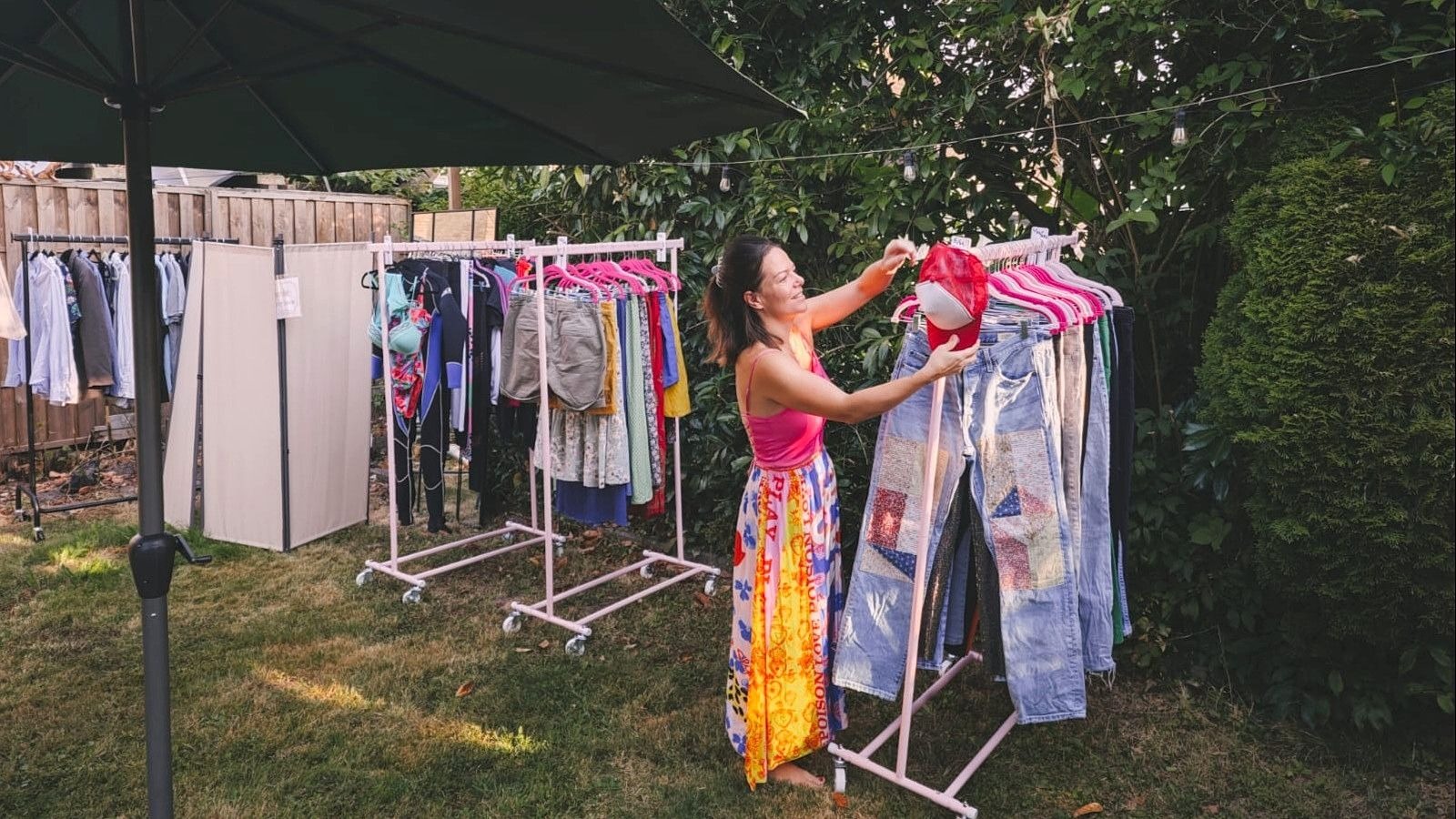 Christin Cornelsen sortiert eine rote Mütze an einem Ständer voller Second-Hand-Kleidung in einem Garten
