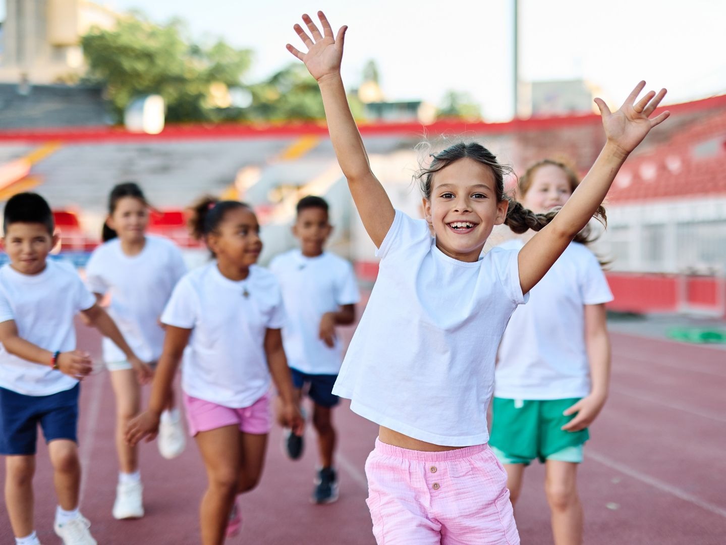 Gruppe Kinder in weißen T-Shirts jubelt mit erhobenen Armen auf einer roten Laufbahn