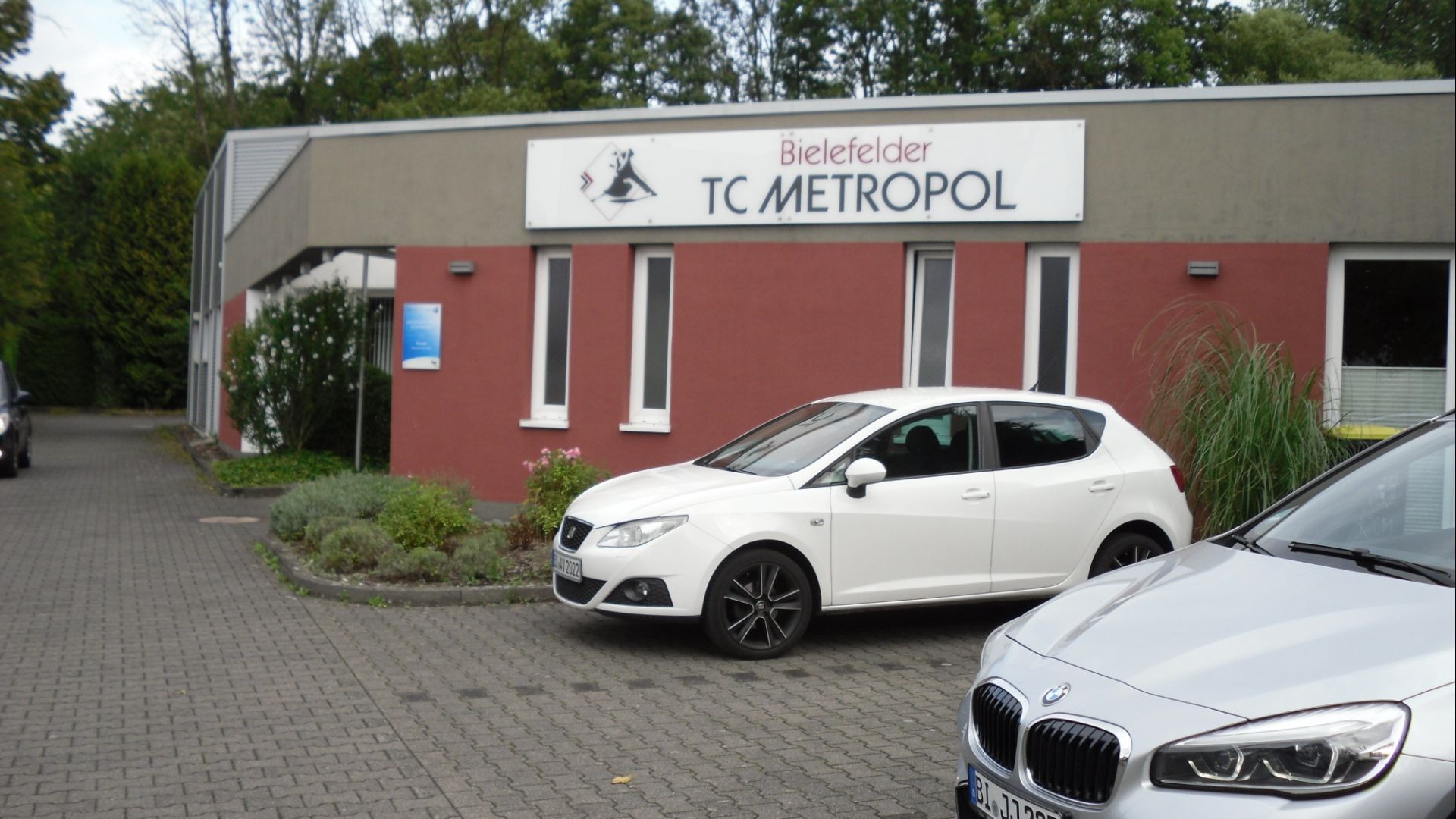 Das Gebäude des Bielefelder TC Metropol mit Schild, roten Wänden und zwei geparkten Autos auf einem gepflasterten