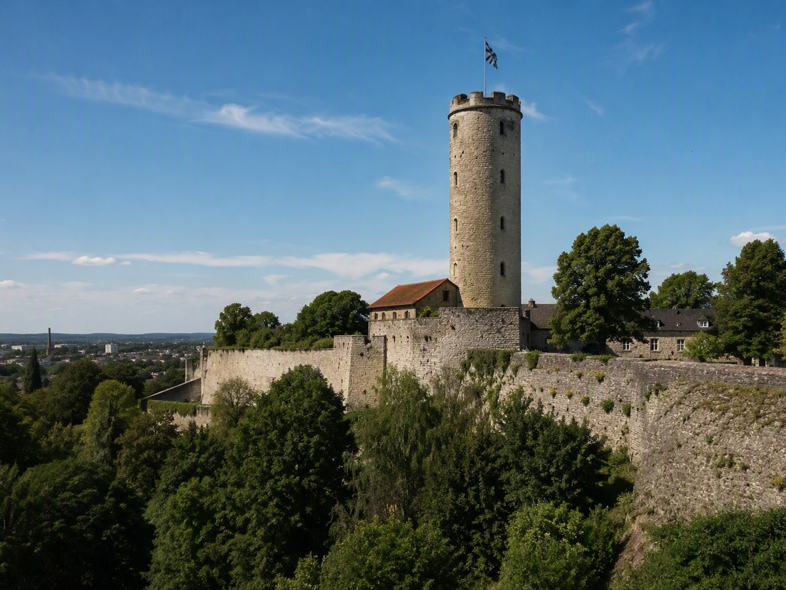 Hoher runder Steinturm der Sparrenburg in Bielefeld mit Fahne, umgeben von historischen Mauern und Bäumen bei blauem