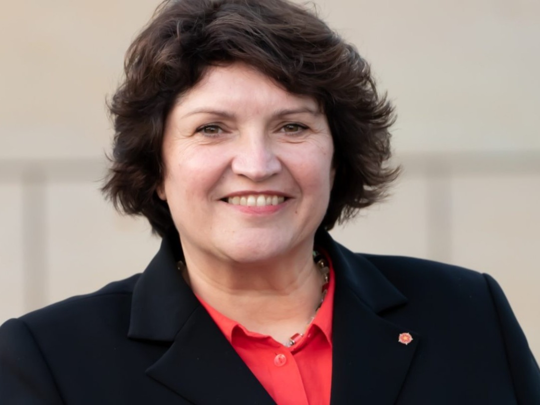 Lächelnde Landtagsabgeordnete mit kurzen, dunklen Haaren, rotem Hemd und dunklem Blazer