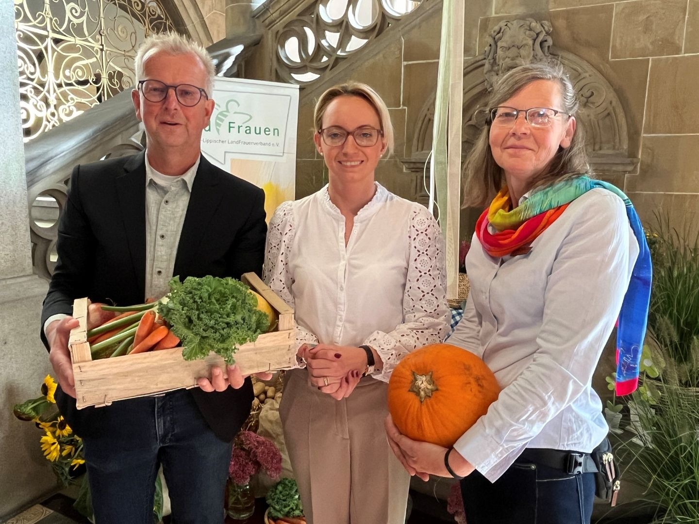 Drei Personen präsentieren Gemüse und Kürbis vor dem Alten Rathaus und einem Banner der Landfrauen