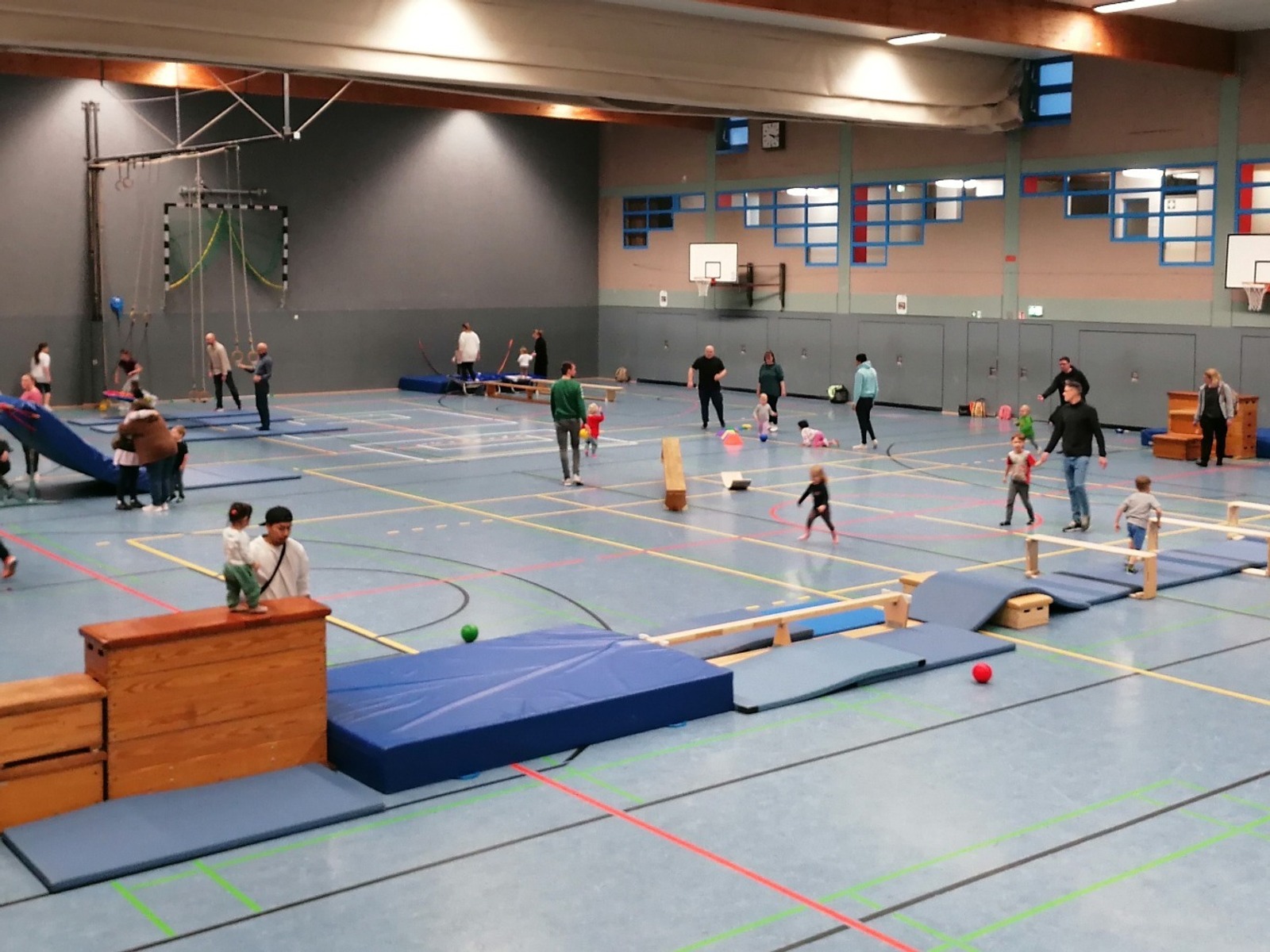 Viele Erwachsene und Kinder spielen und bewegen sich in einer Sporthalle mit aufgebautem Parcours aus Turngeräten und