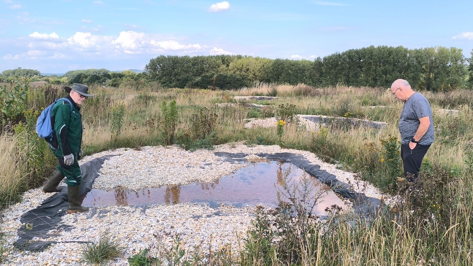 Zwei Männer in einem Feld begutachten mehrere kleine, mit Kies ausgekleidete Wasserbecken