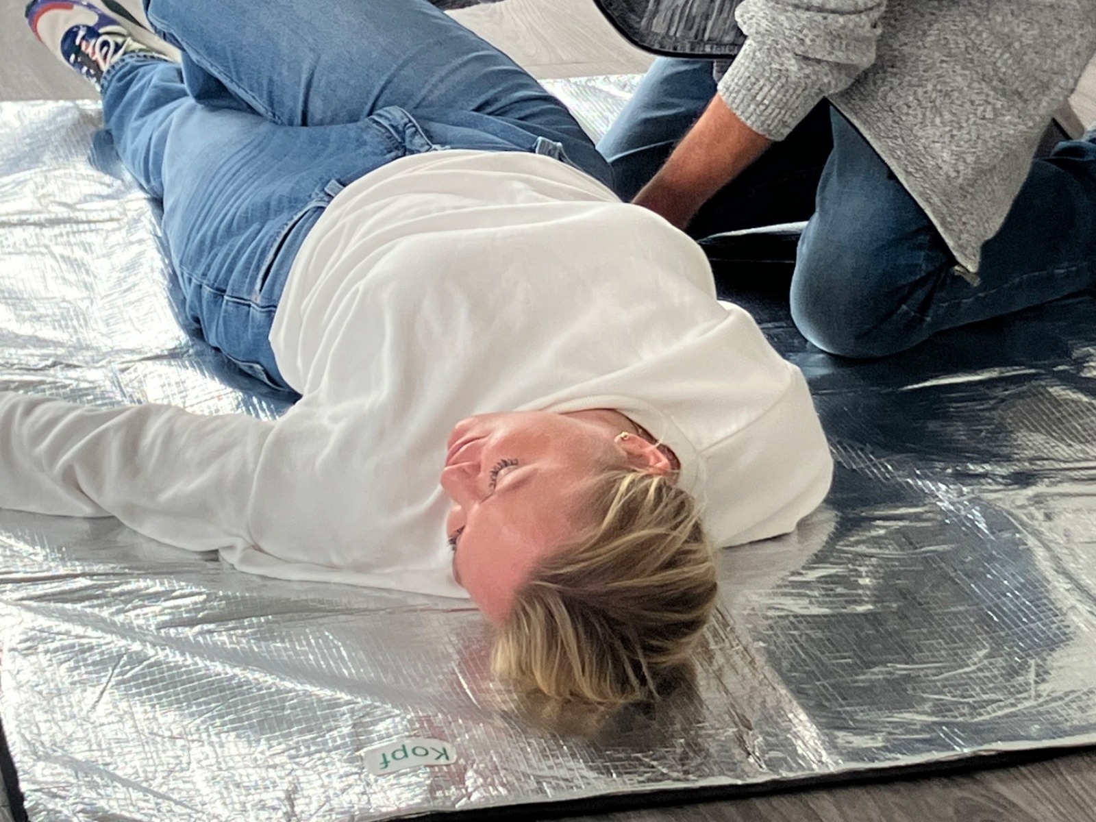 Ein Mann übt die stabile Seitenlage an einer Frau, die auf einer silbernen Rettungsdecke liegt