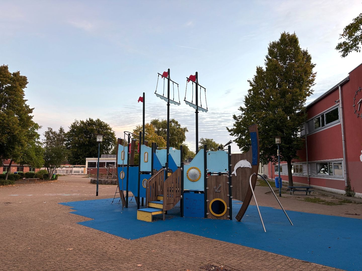 Großes blau-braunes Spielschiff "NORDSTERN" mit roten Flaggen auf dem Schulhof vor dem roten Gebäude der Grundschule