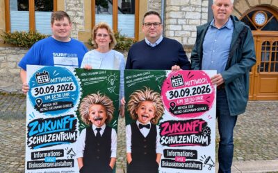 Vier Personen stehen vor einem Gebäude und halten zwei Plakate zur Zukunftsplanung Schulzentrum, darauf ein Kind mit