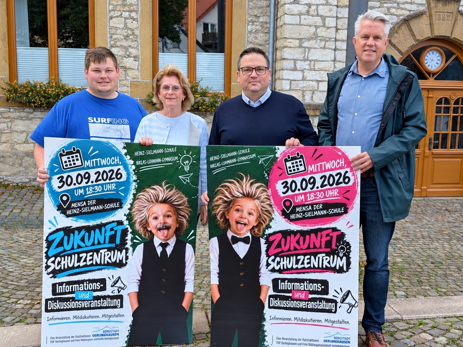 Vier Personen stehen vor einem Gebäude und halten zwei Plakate zur Zukunftsplanung Schulzentrum, darauf ein Kind mit
