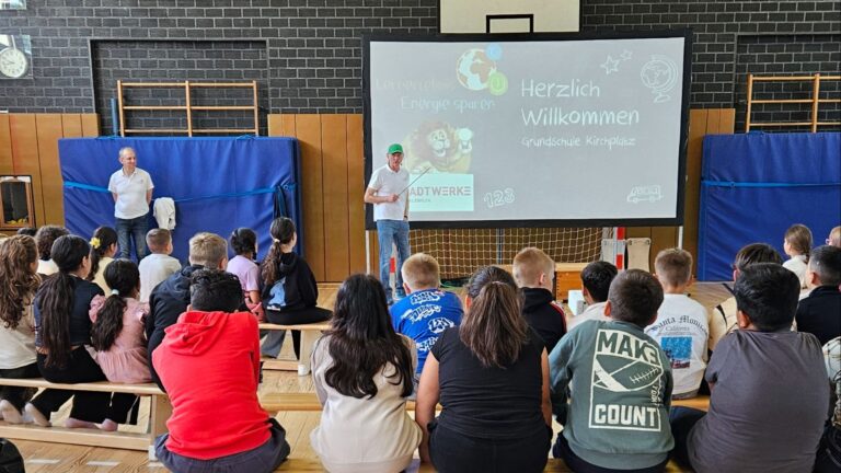 Kinder in einer Turnhalle schauen einem Mann bei der Energiespar-Präsentation der Stadtwerke Bad Salzuflen zu