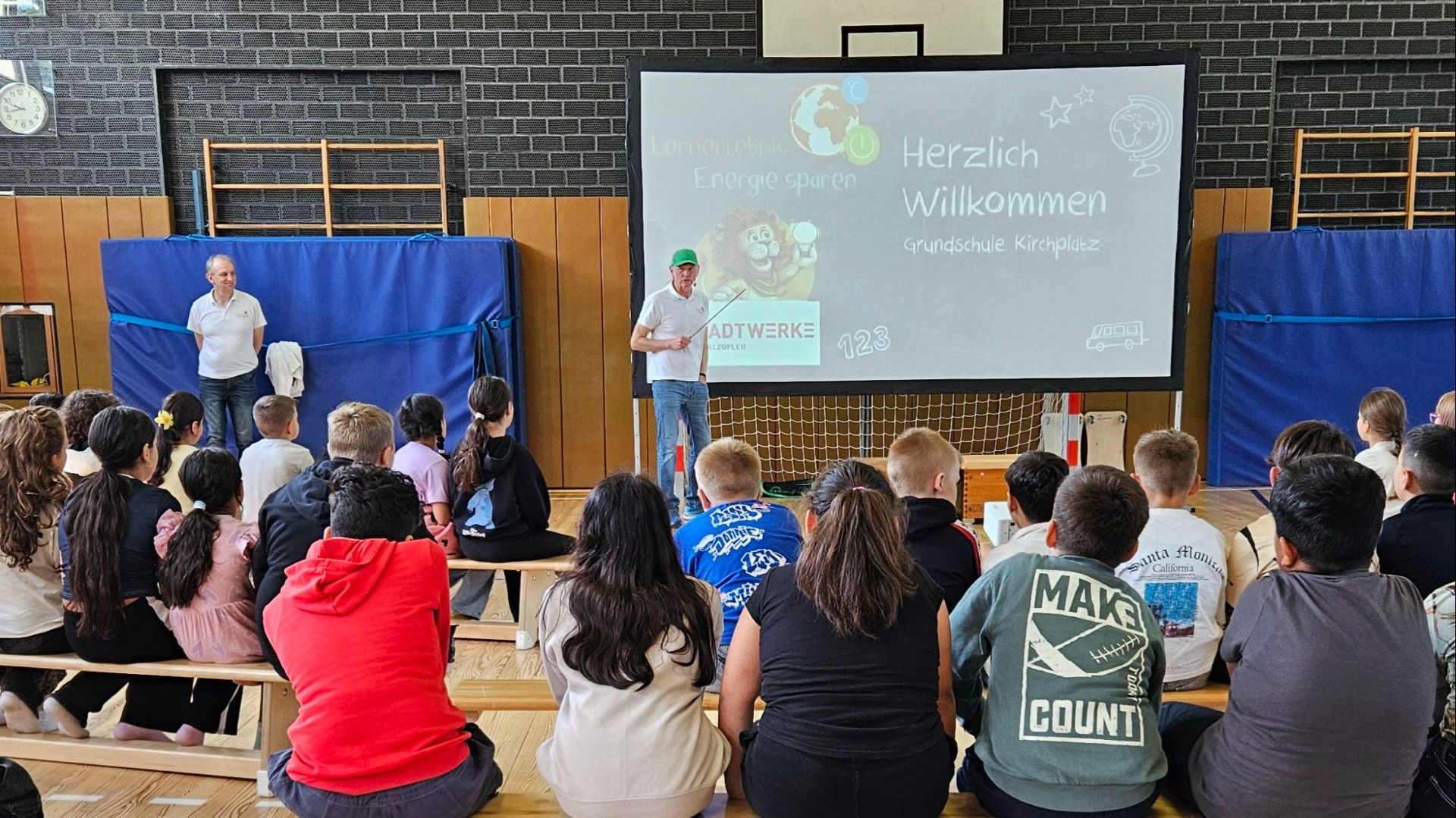 Kinder in einer Turnhalle schauen einem Mann bei der Energiespar-Präsentation der Stadtwerke Bad Salzuflen zu
