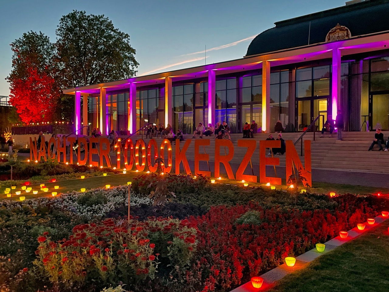 Abendliche Szene im Kurpark mit beleuchtetem Gebäude, dem Schriftzug NACHT DER 100000 KERZEN, vielen Lichtern und