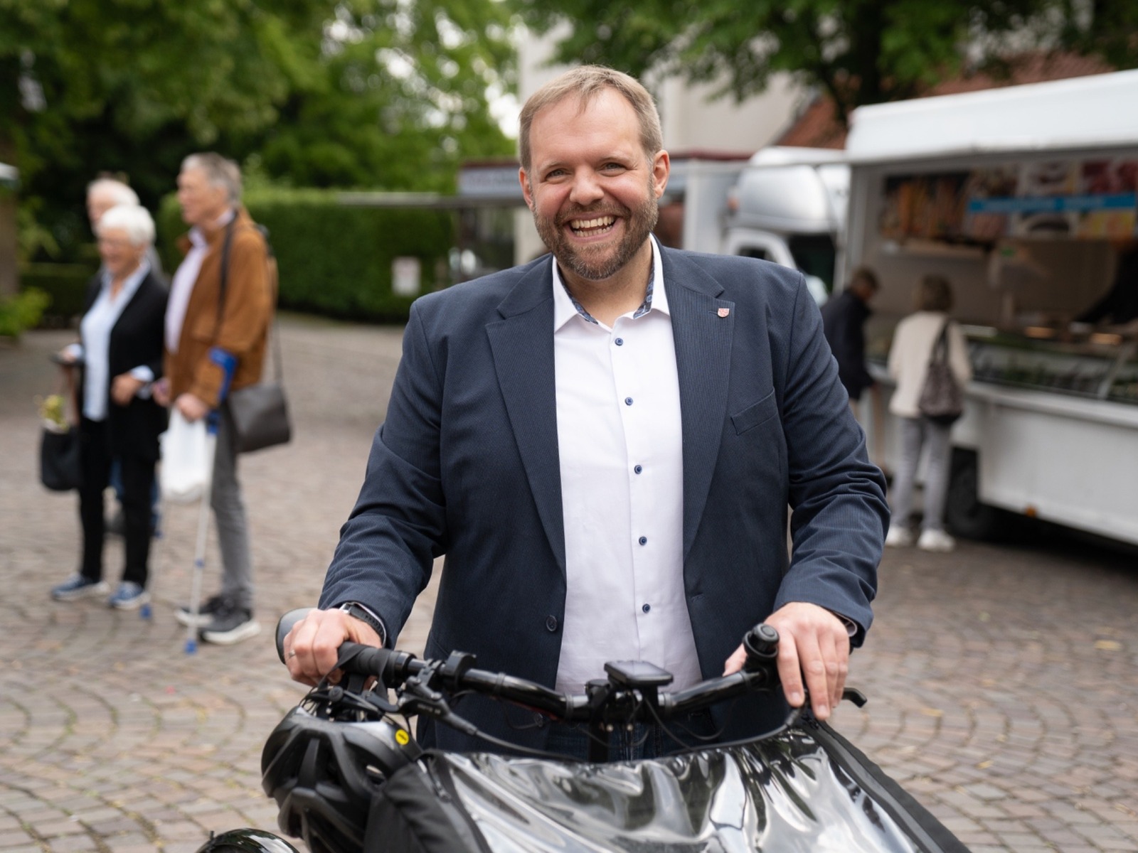 Lemmen lacht breit, hält die Lenker eines Lastenrads, hinter ihm Menschen und ein Imbisswagen