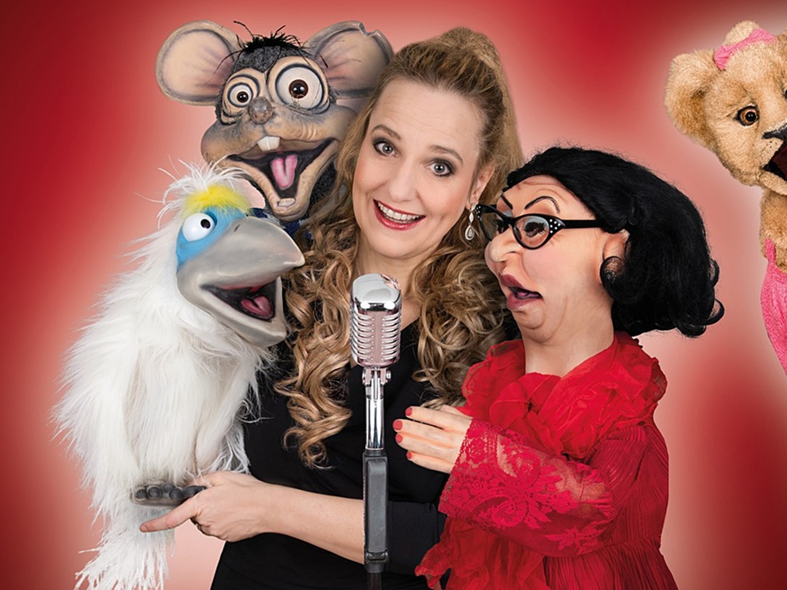 Murzarella lächelt mit einem Mikrofon und vier Puppen: einem Vogel, einer Ratte, einer Dame und einem Löwen