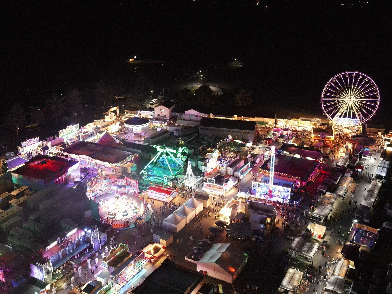 Luftaufnahme des hell beleuchteten Wilbaser Marktes bei Nacht mit Riesenrad, Fahrgeschäften und vielen Besuchern