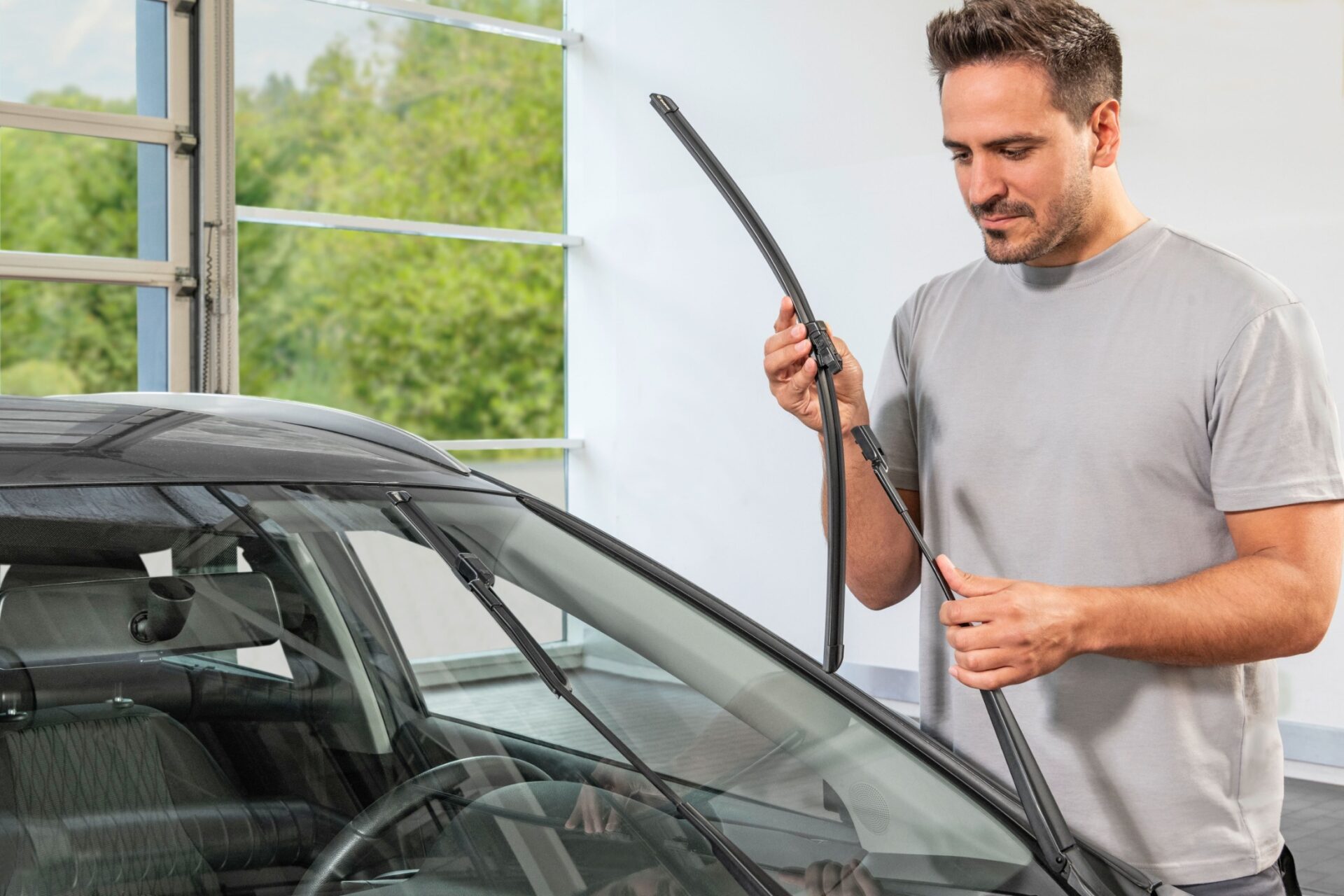 Mann tauscht Scheibenwischer an der Frontscheibe eines schwarzen Autos