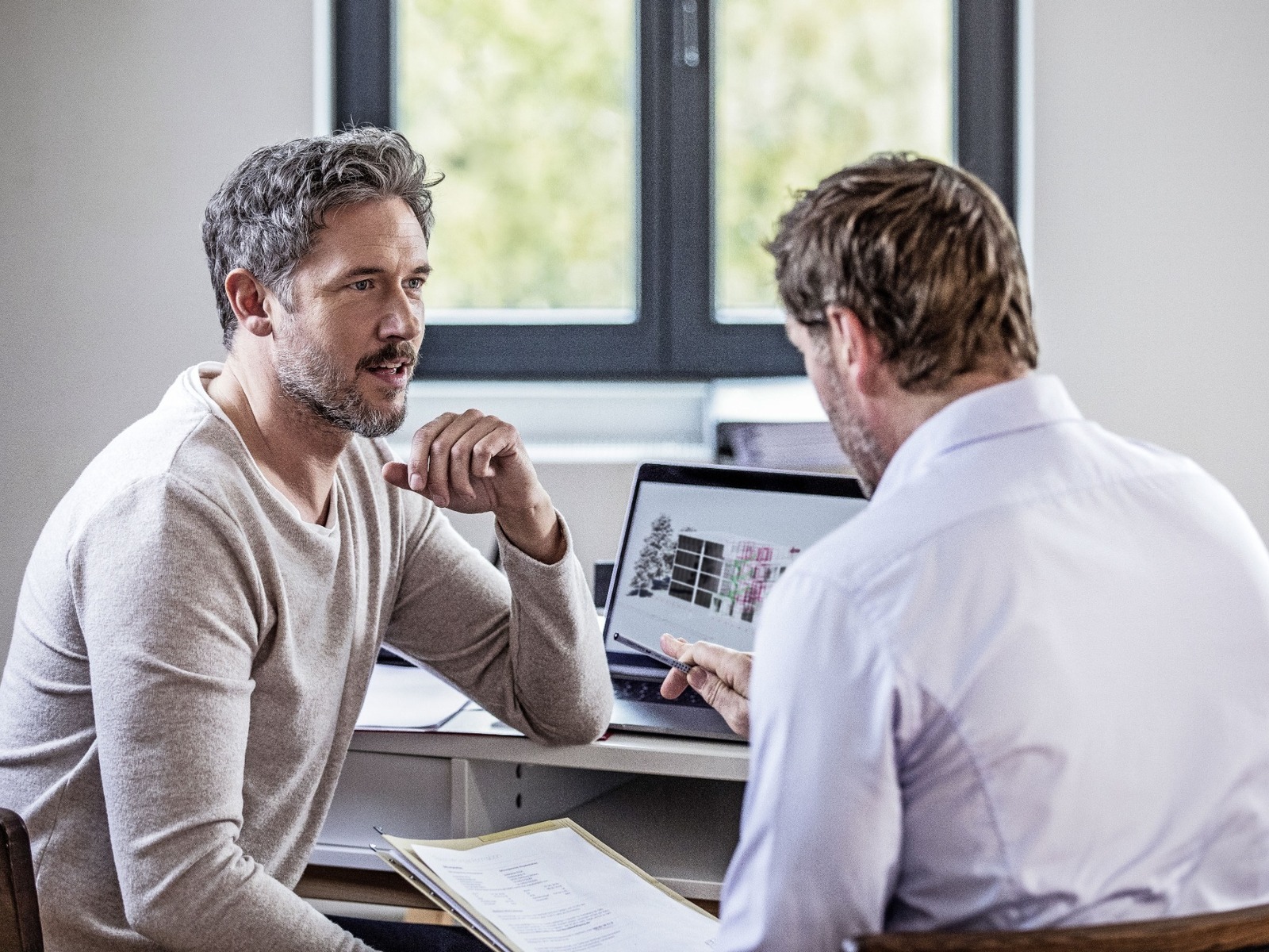 Zwei Männer besprechen an einem Laptop einen Entwurf zur Haussanierung, einer zeigt auf den Bildschirm