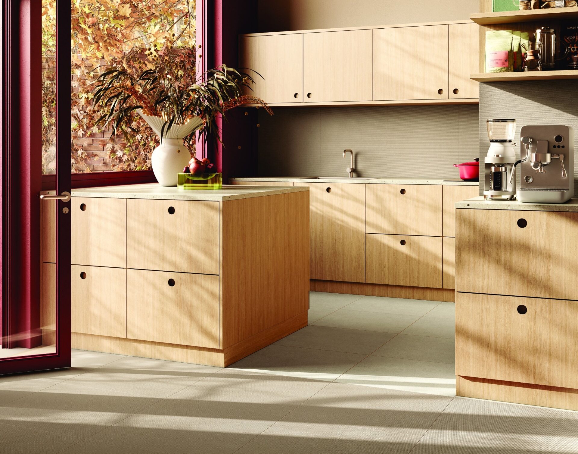 Moderne Küche mit hellen Holzmöbeln, hellem Fliesenboden, Kaffeemaschine und Fenster mit Herbstlaub im Sonnenlicht