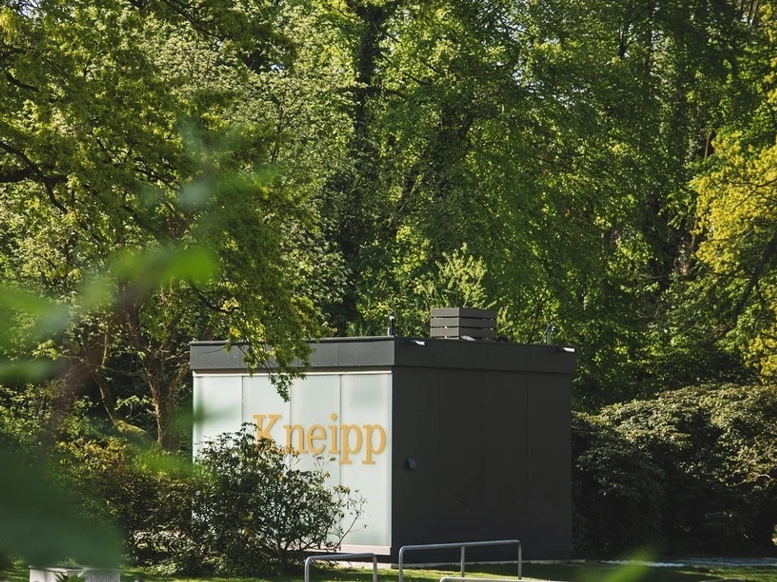 Modernes Kneipp-Gebäude mit Schriftzug umgeben von Bäumen und Büschen im Landschaftsgarten