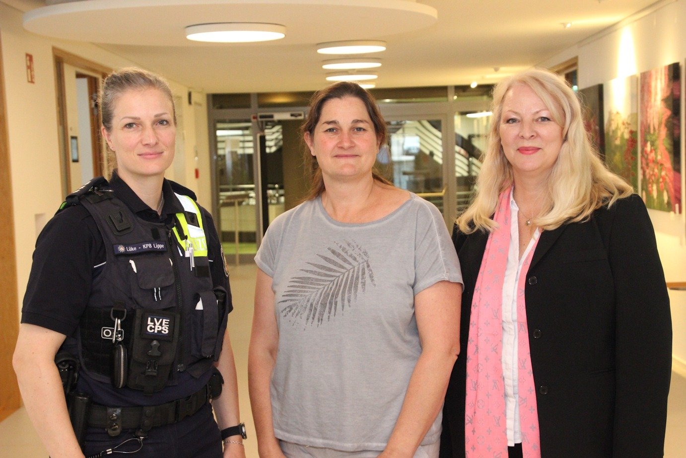 Polizistin Lüke von KPB Lippe, eine Frau in grauem Shirt und eine blonde Frau im Blazer stehen zusammen im Flur