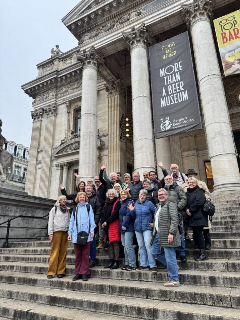Lachende Mitglieder eines Vereins posieren auf einer Treppe vor der säulenreichen Fassade des Belgian Beer World in