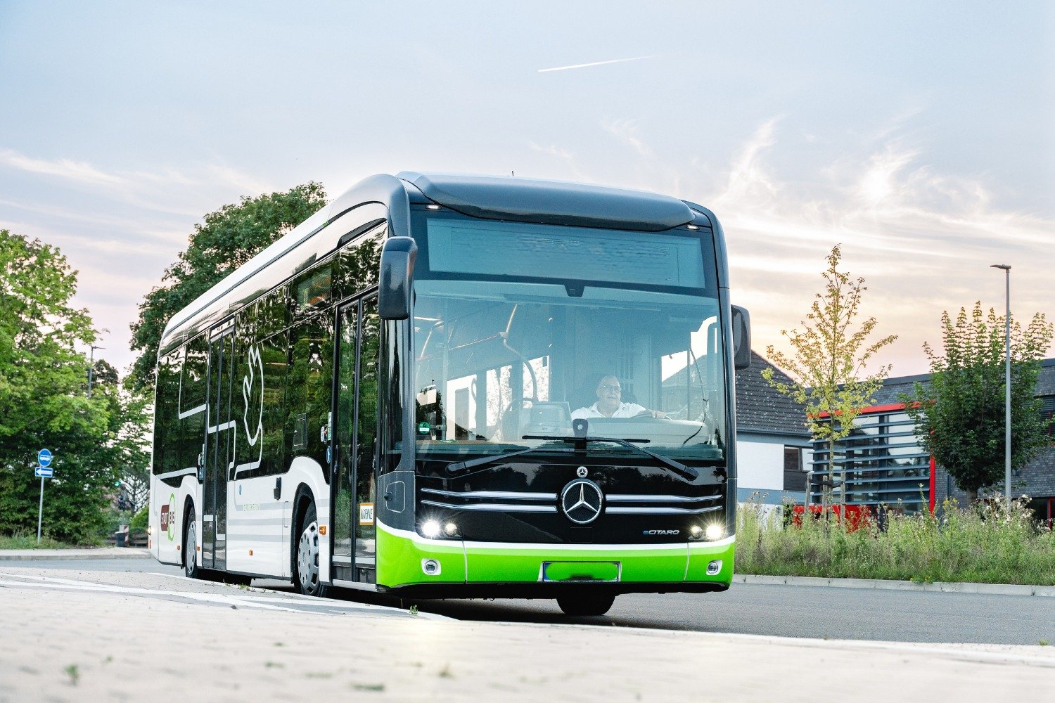 Ein grüner, schwarzer und weißer Mercedes-Benz eCitaro Stadtbus mit Fahrer auf einer Straße