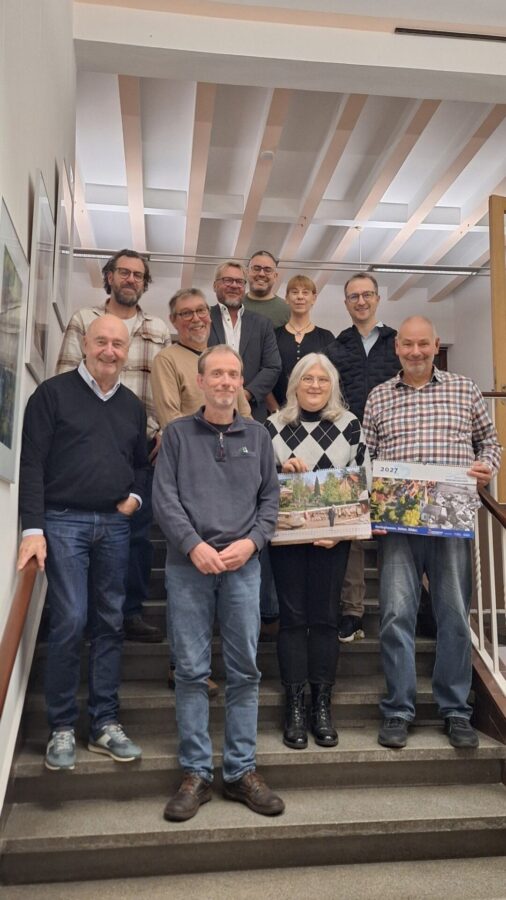 Zehn lächelnde Personen stehen auf einer Treppe und präsentieren zwei Kalender "Oerlinghausen 2027