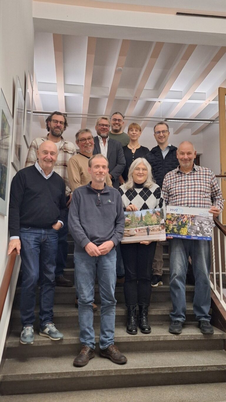 Zehn lächelnde Personen stehen auf einer Treppe und präsentieren zwei Kalender "Oerlinghausen 2027