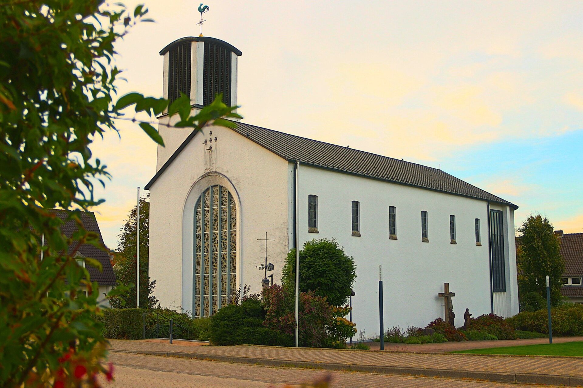 Weiße Kirche mit hohem Turm, großem Buntglasfenster, Wetterhahn und zwei religiösen Kreuzen