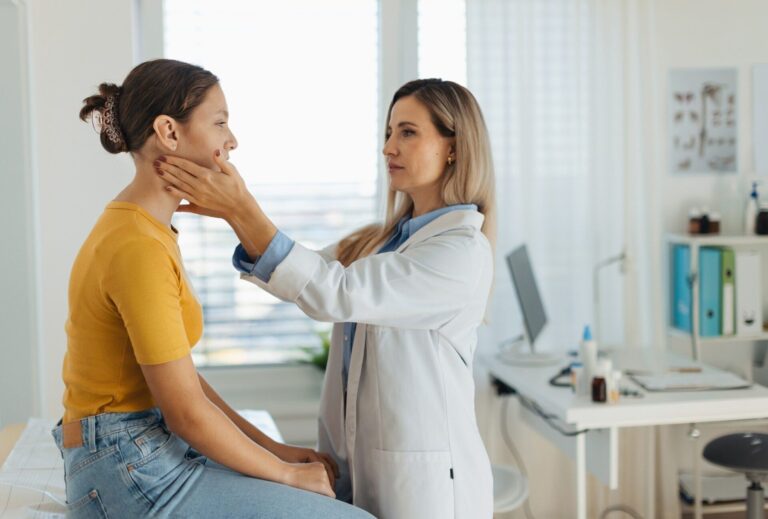 Eine Ärztin im weißen Kittel untersucht den Hals einer jungen Patientin während eines Gesundheitschecks in der Praxis