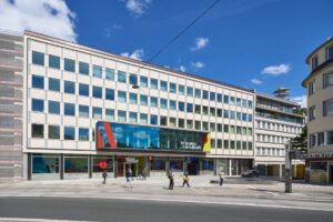 Menschen gehen auf dem Bürgersteig vor dem Gebäude WissensWerkstadt unter blauem Himmel mit einigen Wolken