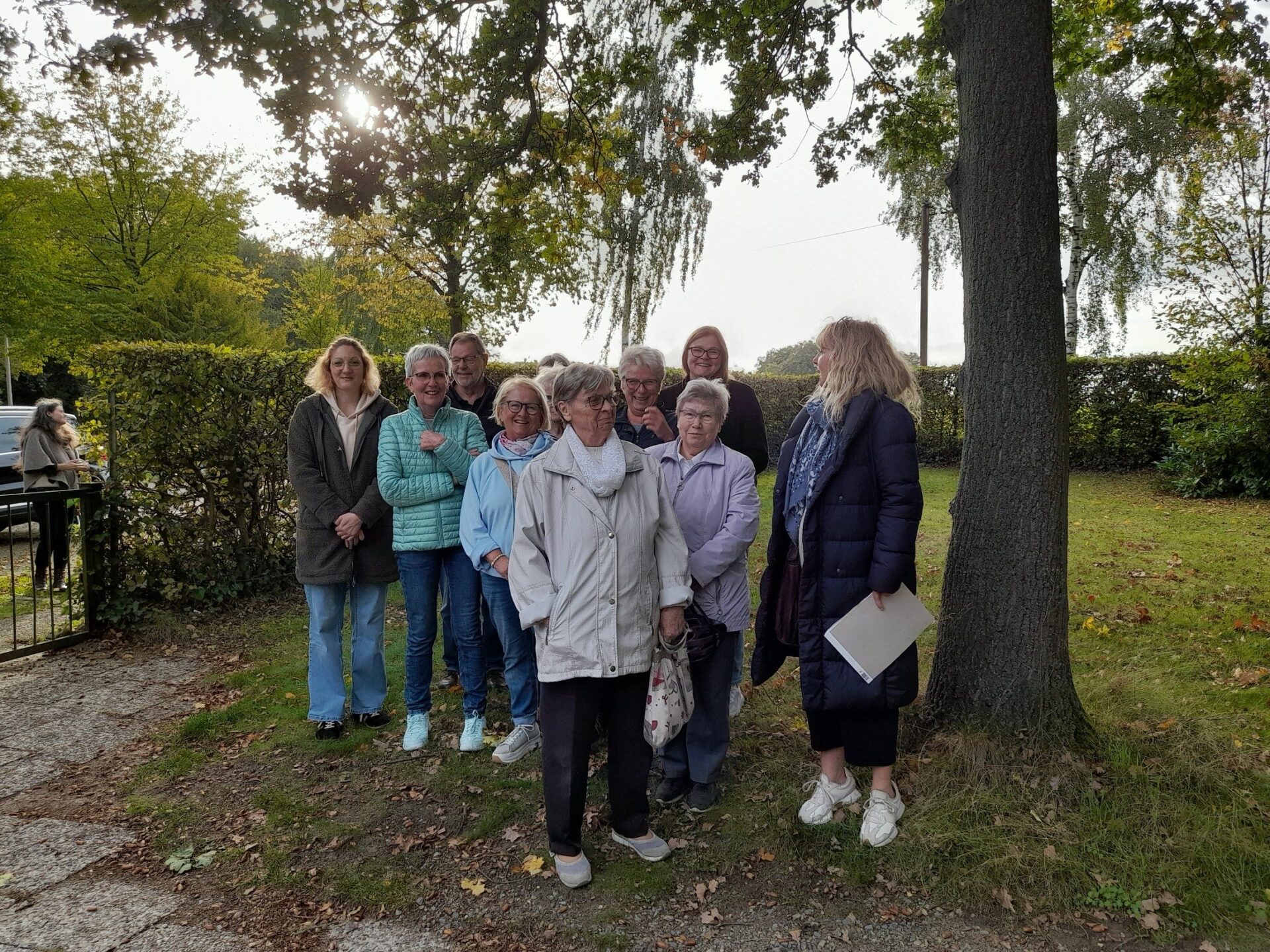 Gruppe von elf Personen, meist ältere Frauen, stehen lächelnd im Freien vor Bäumen und einem Weg
