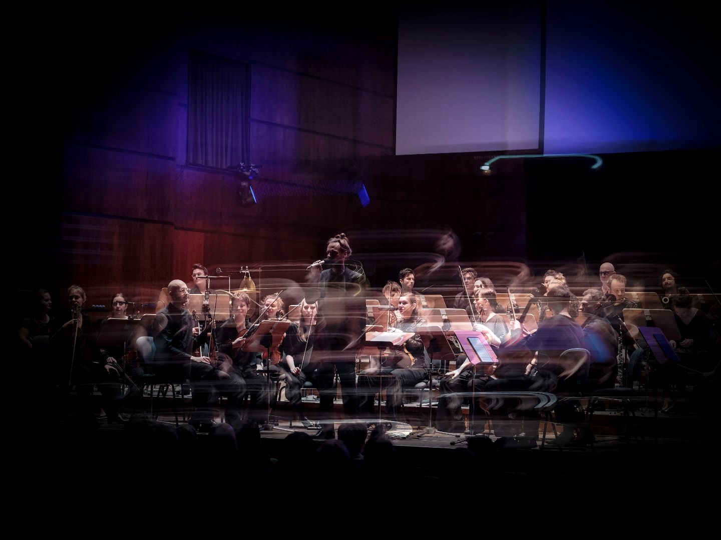 Orchester mit Musikern und einem Sänger auf einer Bühne unter blauer Beleuchtung